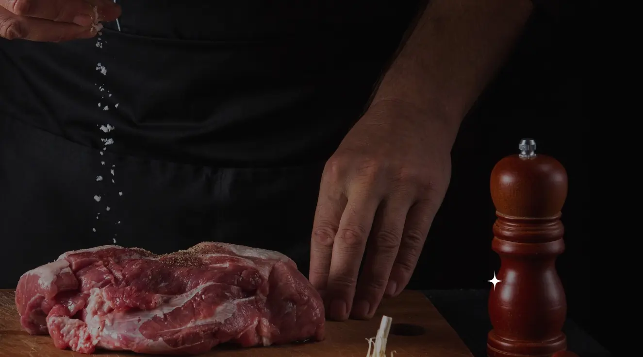 Mains d'un boucher salant une pièce de viande sur une planche